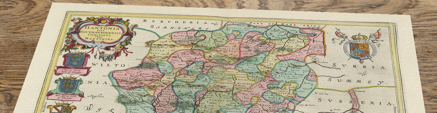 Upper section of Joan Blaeu’s Hampshire map, with its decorative title and royal arms, lying at an angle on a wooden table