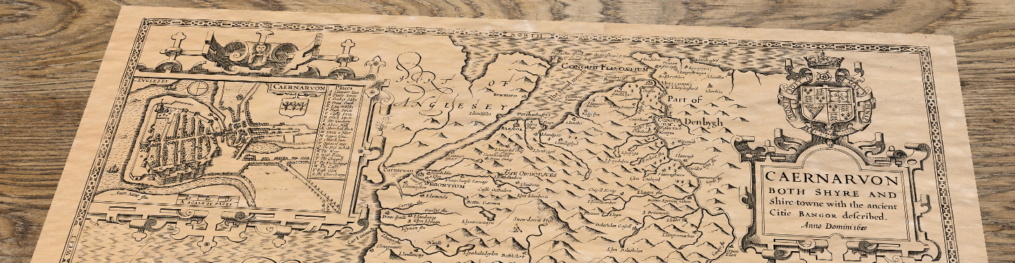 Upper section of Caernarvonshire - an old map by John Speed, lying at an angle on an antique ash table